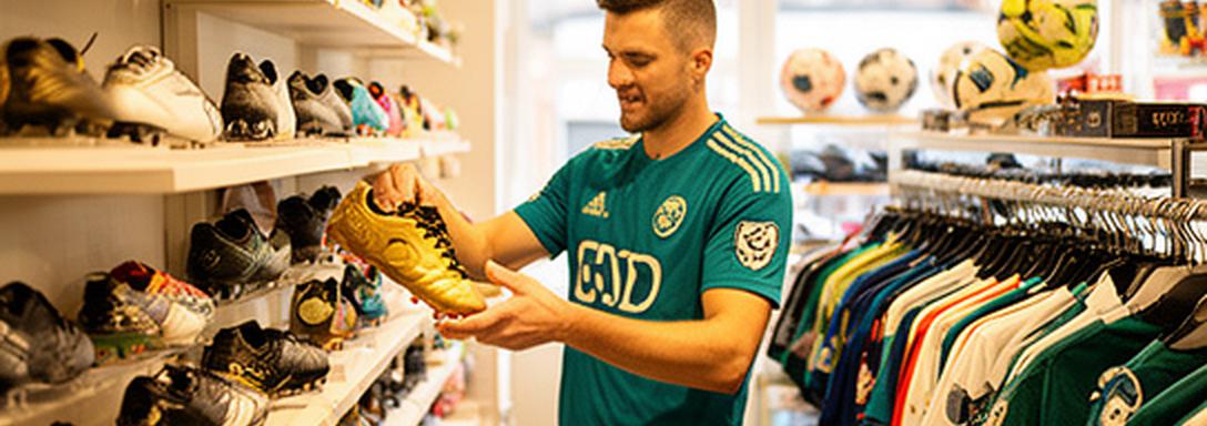 Footballer choosing boots inside a bright Norwich football shop with club shirts on the walls